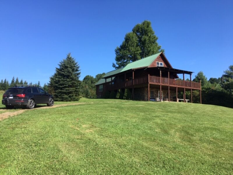 A rental cabin with lush green lawn in front and evergreen trees behind it.